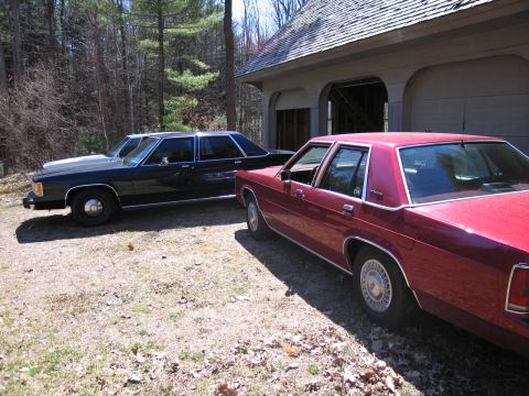 1991 Ford LTD Crown Victoria - Two sedans are parked in front of a garage on a sunny day.