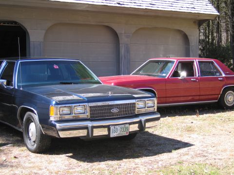 1991 Ford LTD Crown Victoria - Two Ford Crown Victorias are parked outside a garage on a sunny day.