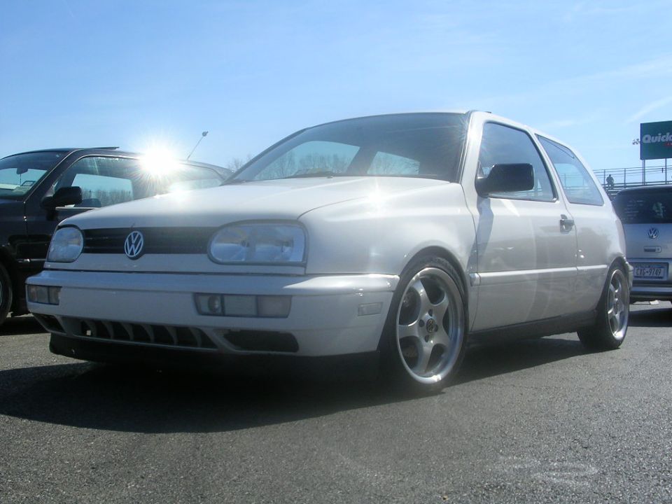 White Volkswagen Golf GTI with aftermarket wheels parked next to another car