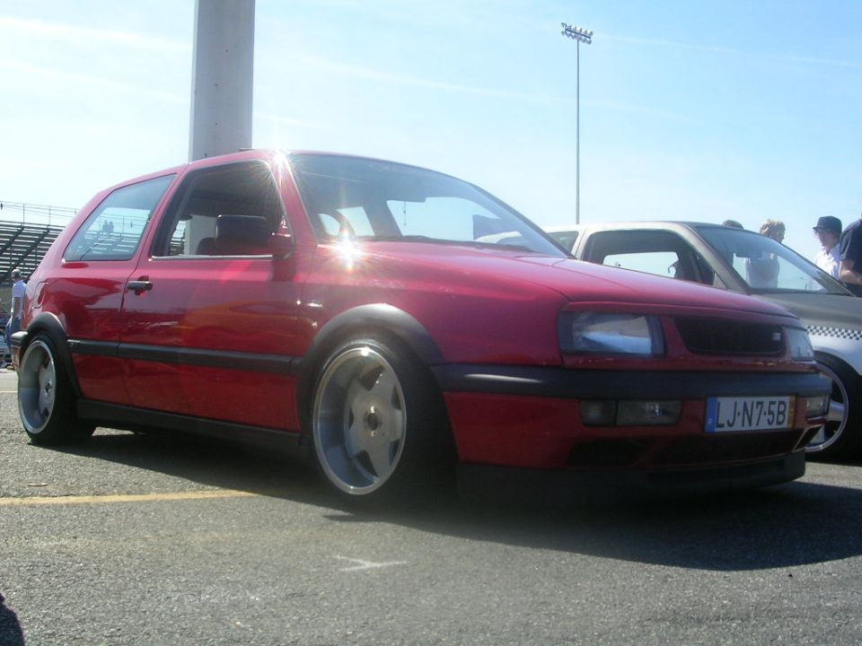 Red hatchback car with custom wheels and lowered suspension, seen from the front-right