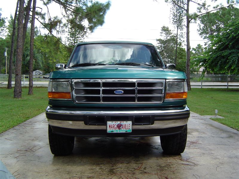 Front view of green Ford truck with chrome bar grille and MARGARITAVILLE plate on a stamped concrete drive