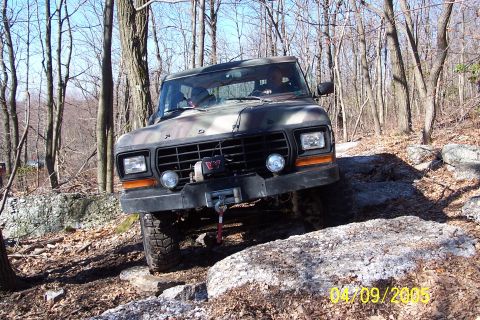 1979 Ford Bronco - A camouflaged Ford Bronco navigates a rocky, wooded trail.