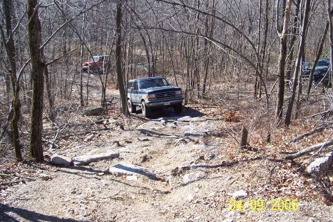1979 Ford Bronco - Multiple off-road vehicles traverse a challenging rocky path through a dense forest.