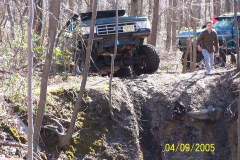 1979 Ford Bronco - Modified 1979 Ford Bronco navigates a steep dirt incline, with another off-road vehicle and a person nearby.