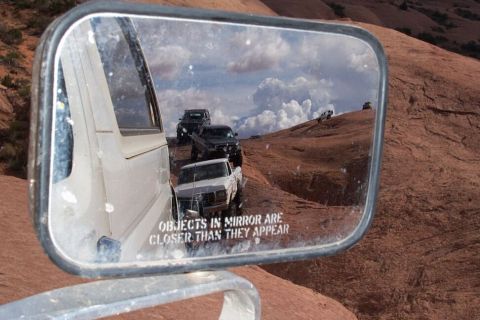 1990 Ford Bronco - Off-road vehicles navigate a rocky trail, as seen in a side mirror reflection. The year is estimated to be around 1980.