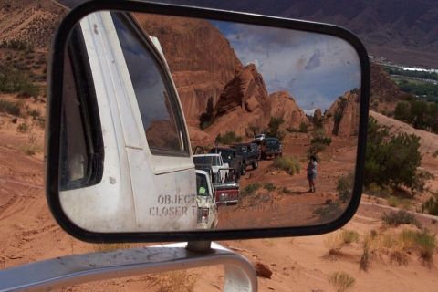 1990 Ford Bronco - A line of off-road vehicles navigates a dusty trail amidst desert scenery, as seen in a side mirror.
