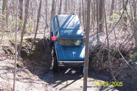 1979 Ford Bronco - A blue 1978 Ford Bronco attempts to traverse a challenging muddy terrain in a wooded area.