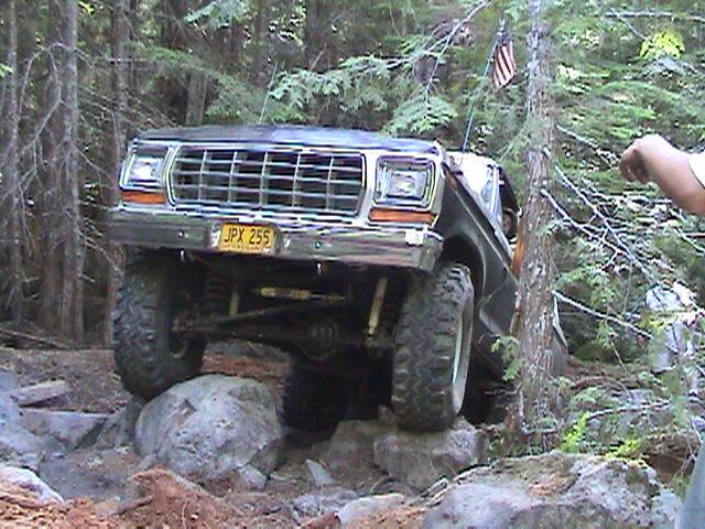 1978 Ford Bronco navigating rocky terrain with an American flag on a tree