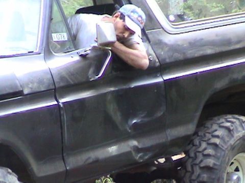 1978 Ford Bronco - A man is seen leaning into the driver's side of a black 1978 Ford Bronco, which has significant damage to the door.