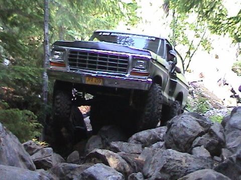 1978 Ford Bronco - This lifted Ford Bronco navigates a rocky trail, with trees and foliage surrounding it.