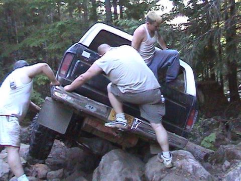 1978 Ford Bronco - Three people attempt to free a stuck SUV from a rocky trail in a wooded area.