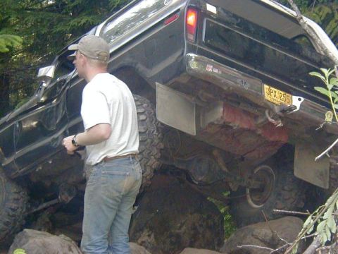 1978 Ford Bronco - A man stands next to a black 1978 Ford Bronco as it navigates rocky terrain.