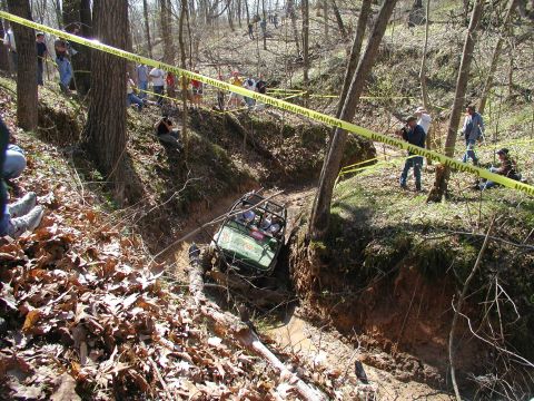 1992 Ford Bronco - An off-road vehicle attempts to traverse a challenging, muddy terrain with spectators observing the event.