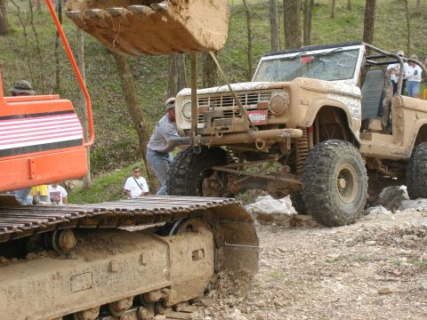 1992 Ford Bronco - An excavator lifts a muddy off-road SUV with a roll cage, while another vehicle is visible in the background.
