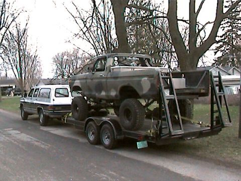 1977 Ford F-150 - Camouflaged 1977 Ford F-150 pickup truck being transported on a trailer, with a white SUV alongside.