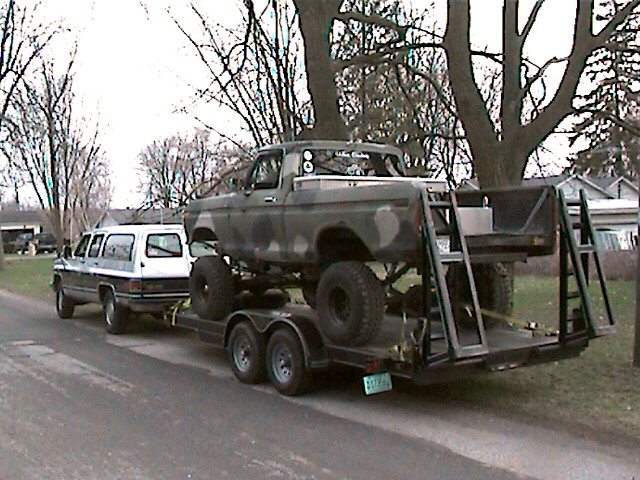 1977 Ford F-150 pickup truck with camouflage paint on a trailer, next to a white SUV