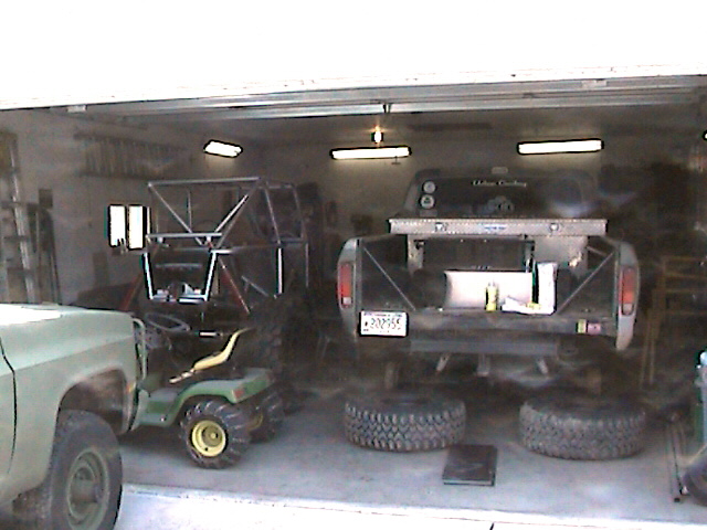1977 Ford F-150 truck bed with custom rack, toolbox, and spare tires. Another vehicle and a lawn tractor are also visible