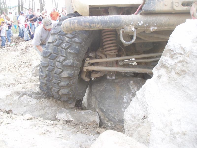 off-road vehicle tire wedged between rocks, people watching