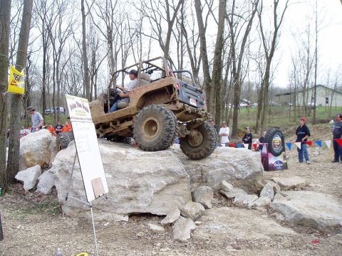 1992 Ford Bronco - An off-road vehicle navigates a challenging rock obstacle course in a wooded area.