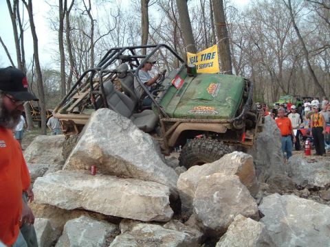 1992 Ford Bronco - A heavily modified off-road vehicle attempts to traverse a challenging rocky terrain with spectators observing.