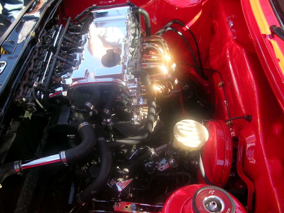 Engine bay with chrome intake manifold and red painted inner fenders. A round headlight is visible