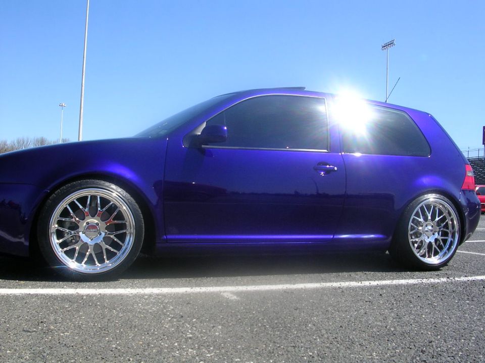 Purple hatchback car with chrome wheels, sun glare on windows, parked on asphalt
