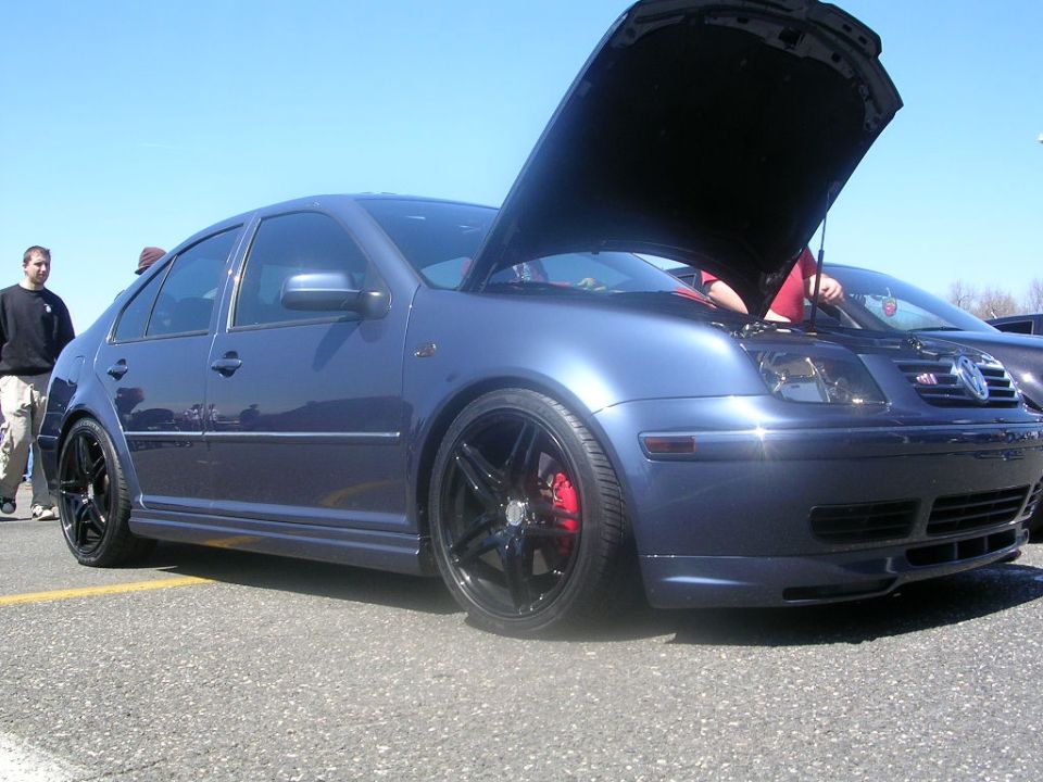 Blue sedan with hood open, red brake calipers, black rims. Another car is visible behind it