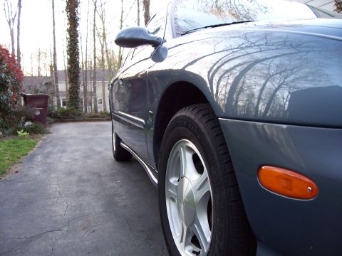 1999 Ford Taurus - The side profile of a sedan shows its front wheel and orange turn signal indicator.