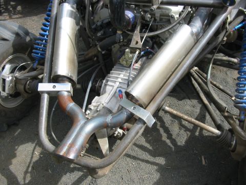1993 Ford Taurus - Close-up of the rear of a tube-frame buggy or sand rail showing twin polished stainless exhaust canisters clamped to a bent header pipe, a…