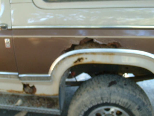 Rusted brown wheel arch and rocker panel of a two-tone tan SUV with worn tire