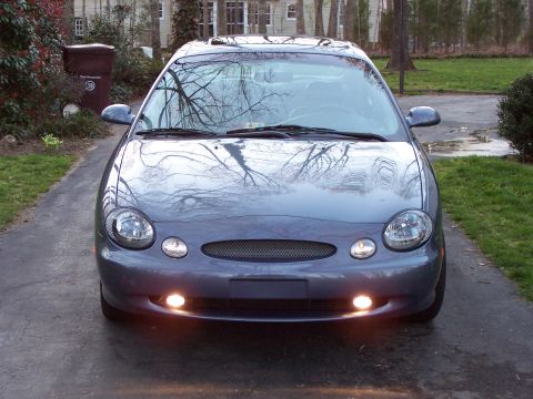 1999 Ford Taurus - A gray sedan is parked in a driveway with trees reflected in its windshield.