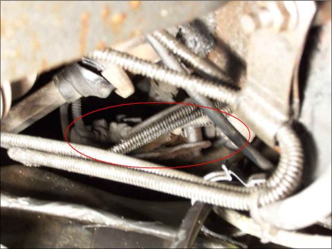 1986 Ford Bronco - Underbody close-up of spring-wrapped steel brake lines running along a frame rail to a junction block, with a red oval drawn on the photo c…
