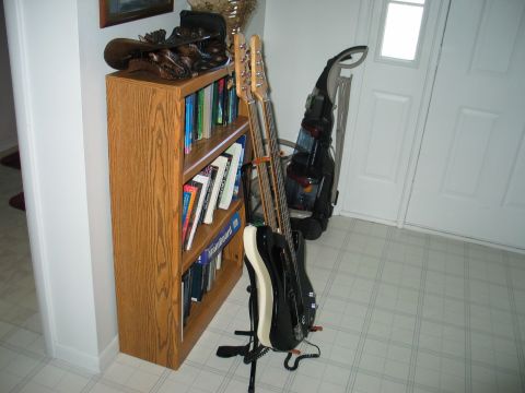 1995 Ford Bronco - A bookshelf filled with books stands next to two guitars and a vacuum cleaner in a hallway.