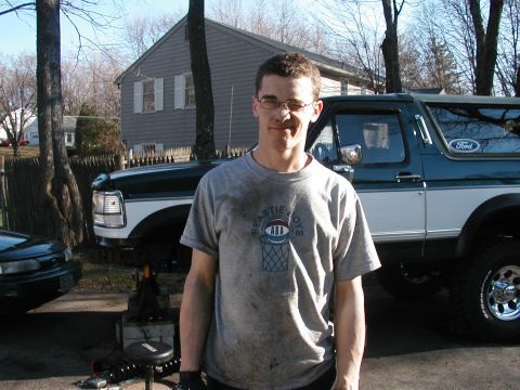 1994 Ford Bronco - Man in a t-shirt stands in front of a Ford Bronco, possibly undergoing maintenance.