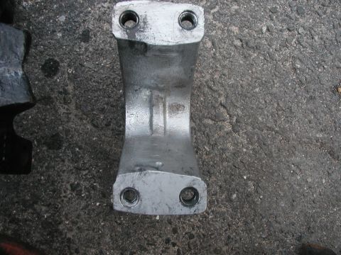 1994 Ford Bronco - A close-up view of a metal bracket with two bolt holes on each end, placed on a rough asphalt surface.