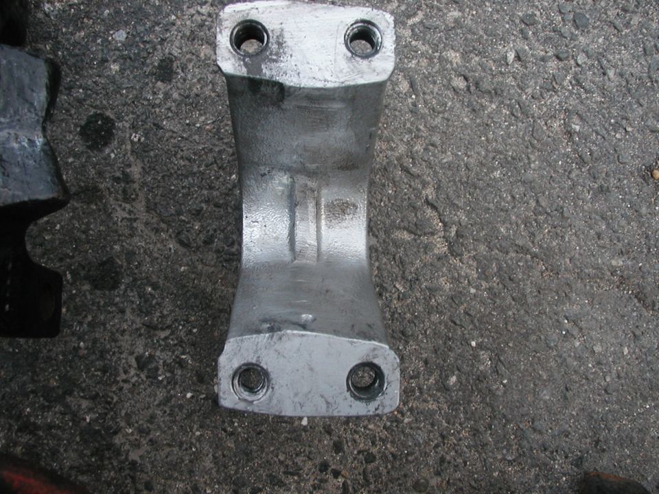 metal bracket with two bolt holes on each end, resting on asphalt