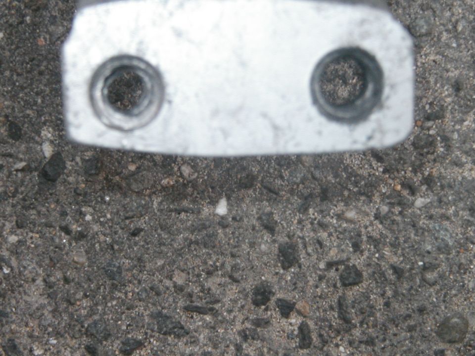 Metal bracket with two circular bolt holes against asphalt