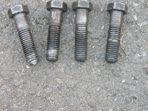 1994 Ford Bronco - Four bolts are shown lying on a textured asphalt surface.