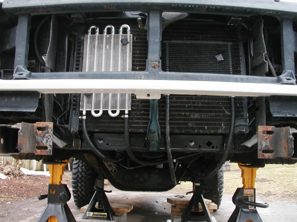Front end of a 1990s Ford Bronco on jack stands, showing the grille, radiator, and an aftermarket transmission cooler