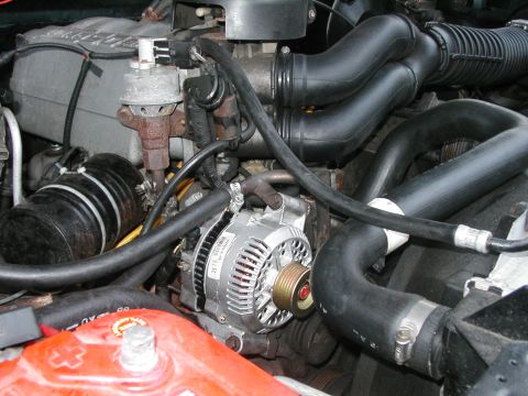 1994 Ford Bronco - Close-up view of an engine bay, highlighting the alternator, various hoses, and a battery.