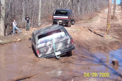 1979 Ford Bronco - Two SUVs navigate a muddy off-road course, with one vehicle deeply mired in the thick mud.
