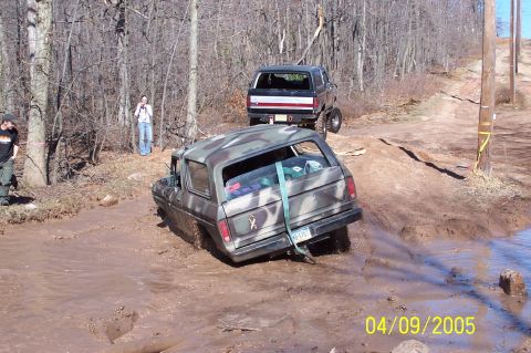 1979 Ford Bronco - Two Ford Broncos navigate a muddy off-road course, one deeply stuck.
