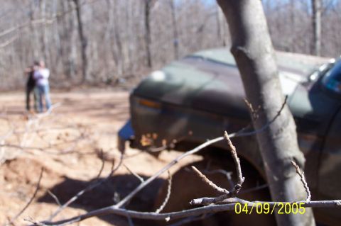 1979 Ford Bronco - A camouflage SUV is seen off-road, with a tree trunk obscuring part of its front.
