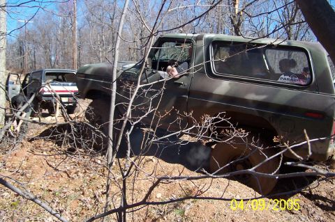 1979 Ford Bronco - A 1979 Ford Bronco in camouflage paint is seen off-roading through a wooded area, with another vehicle visible in the background.