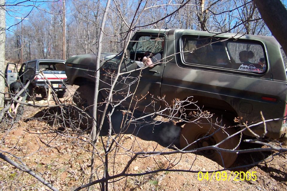 Camouflage 1979 Ford Bronco navigating rough terrain with another vehicle behind