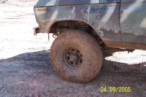 1979 Ford Bronco - Muddy tire and fender of a camouflaged vehicle on rough terrain.