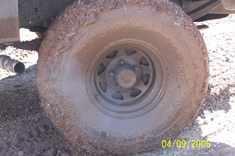 1979 Ford Bronco - A close-up view of a vehicle's tire and suspension covered in mud.