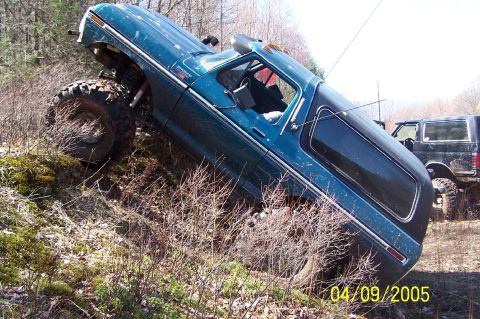 1979 Ford Bronco - A blue 1978 Ford Bronco navigates a steep, wooded incline, with another SUV visible in the background.