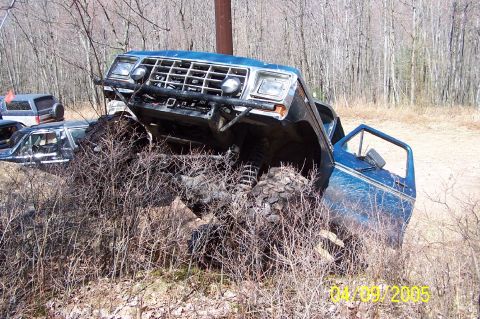 1979 Ford Bronco - Modified 1979 Ford Bronco attempting an off-road obstacle, with other vehicles nearby.