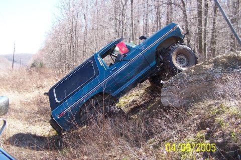 1979 Ford Bronco - A blue SUV navigates a challenging rocky terrain off-road.